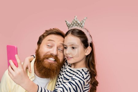 Téléchargez les photos : Preteen fille avec couronne bandeau prendre selfie avec gai père isolé sur rose - en image libre de droit