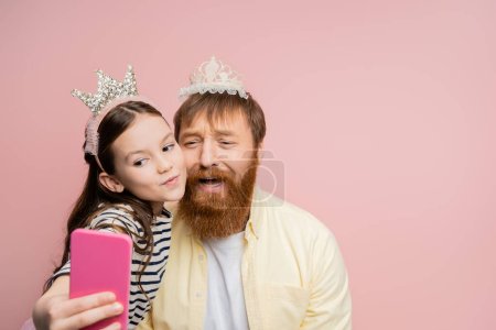 Foto de Preadolescente chica tomando selfie con triste papá con corona diadema aislado en rosa - Imagen libre de derechos
