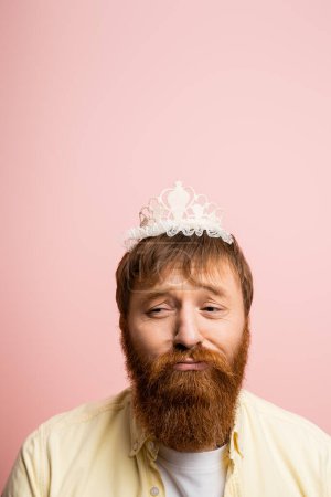Téléchargez les photos : Homme barbu bouleversé avec bandeau couronne fronçant les sourcils isolé sur rose - en image libre de droit