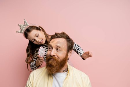 Photo for Smiling girl with crown headband holding brush near bearded father isolated on pink - Royalty Free Image