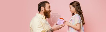 Photo for Side view of tattooed father giving present to daughter isolated on pink, banner - Royalty Free Image