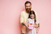Smiling bearded man giving gift box to daughter on pink background  magic mug #645841150