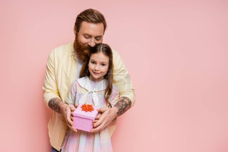 Overjoyed man holding present near preteen child on pink background 