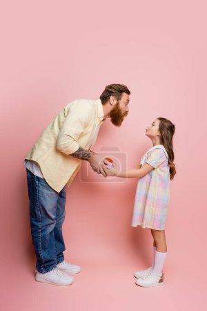 Téléchargez les photos : Vue latérale de l'homme boudant lèvres tout en donnant boîte cadeau à la fille sur fond rose - en image libre de droit