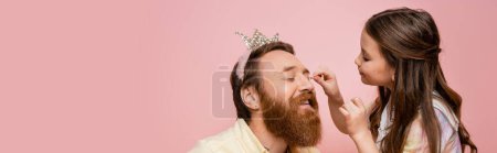 Child applying eyeshadow on bearded dad with crown on head isolated on pink, banner 