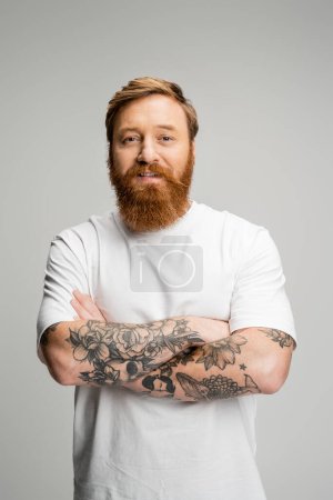 Overjoyed tattooed man looking at camera isolated on grey 