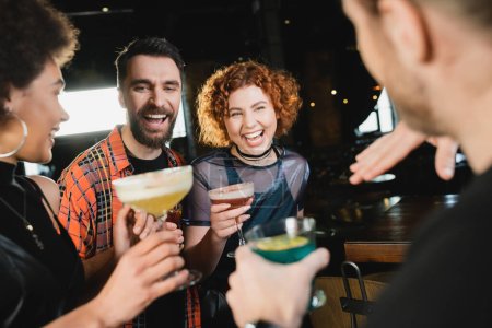 Cheerful multiethnic friends with cold cocktails talking while meeting in bar 