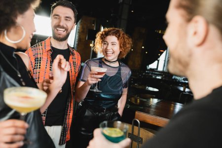 Amigos multiétnicos positivos con diferentes cócteles que se reúnen en el bar por la noche 