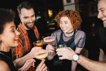 Overjoyed multiethnic friends toasting with different cold cocktails in bar 