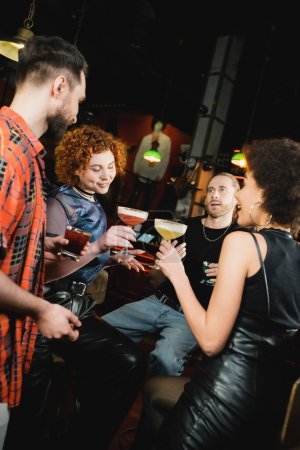 Multiethnic friends holding different cold cocktails while talking in bar 