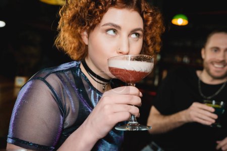 Jeune femme rousse boire cocktail mousse dans le bar 