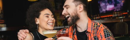 Fröhlicher Mann umarmt afrikanisch-amerikanischen Freund mit Cocktail in Bar, Banner 