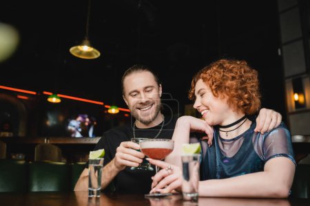 Foto de Amigos positivos tintinean cócteles cerca de tragos de tequila con lima fresca en el bar - Imagen libre de derechos