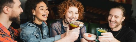 Positive multiethnic people holding different cocktails while clinking in bar, banner 