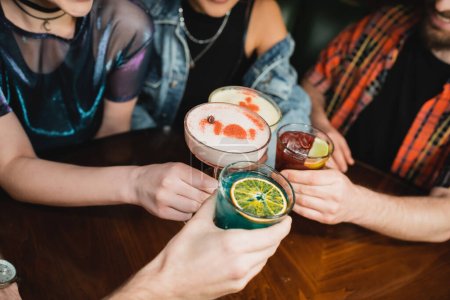 Cropped view of interracial people clinking cocktails in bar in evening 