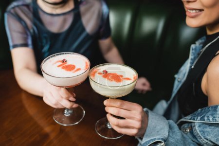 Cropped view of interracial girlfriends holding foam cocktails in bar 