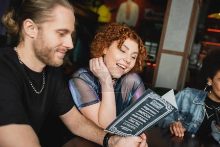 Lächelnde Freunde schauen auf Speisekarte, während sie sich abends in der Bar treffen 