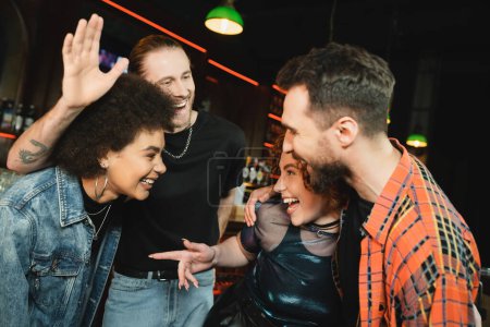 Excited man waving hand near interracial friends while spending time in bar at night 