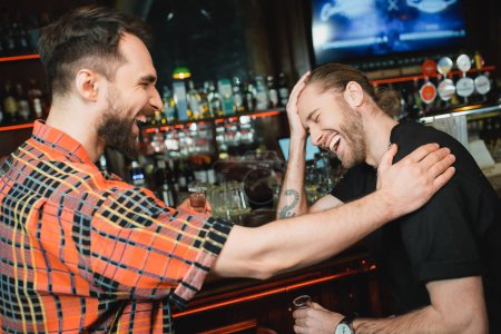 hommes barbus joyeux tenant des coups de tequila tout en riant dans le bar en soirée 