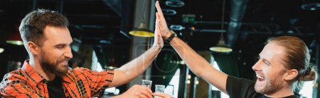 Photo for Cheerful bearded men holding tequila and giving high five in bar, banner - Royalty Free Image