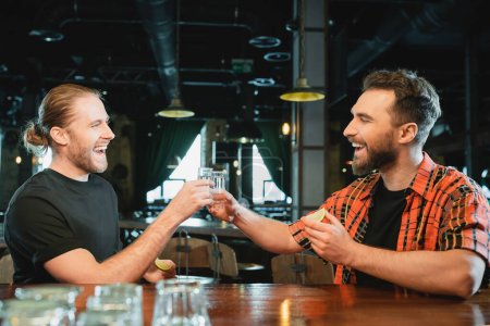 alegres amigos masculinos sosteniendo tiros de lima y tequila en el bar 