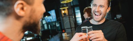 Photo for Excited man clinking tequila with blurred friend in bar, banner - Royalty Free Image