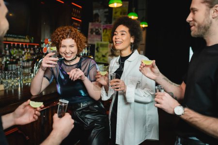 Fröhliche multiethnische Menschen haben Spaß und halten Tequila-Shots in der Bar 