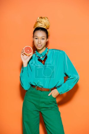Foto de Sonriente modelo afroamericano en traje de verano con pomelo sobre fondo naranja - Imagen libre de derechos