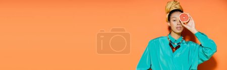 Fashionable african american woman holding grapefruit on orange background, banner 