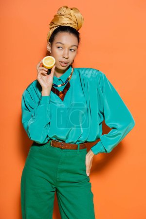 Trendy african american woman holding lemon and posing on orange background 