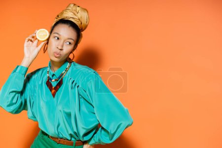 Stilvolles afrikanisch-amerikanisches Model schmollt Lippen und hält geschnittene Zitrone auf orangefarbenem Hintergrund 