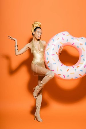 Alegre modelo afroamericano en traje de baño de moda celebración de anillo de piscina sobre fondo naranja 