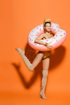 Téléchargez les photos : Femme afro-américaine à la mode et souriante en maillot de bain tenant une bague de piscine sur fond orange - en image libre de droit