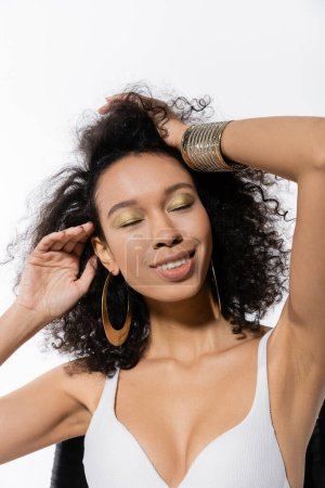 Téléchargez les photos : Modèle afro-américain avec les yeux fermés ajustant les cheveux bouclés isolés sur blanc - en image libre de droit