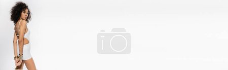 Téléchargez les photos : Modèle afro-américain bouclé en maillot de bain blanc posant sur fond gris, bannière - en image libre de droit
