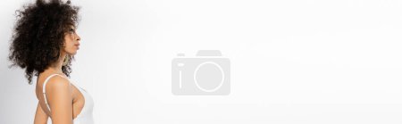 Téléchargez les photos : Vue latérale du jeune modèle afro-américain aux cheveux bouclés posant en maillot de bain blanc sur fond gris, bannière - en image libre de droit