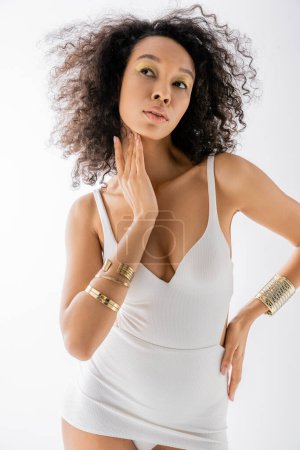 portrait of young african american model with curly hair posing with hand on hip isolated on grey 