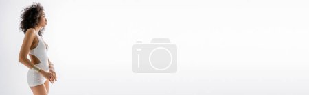 Téléchargez les photos : Vue latérale du modèle afro-américain bouclé en mini-robe serrée debout sur fond gris, bannière - en image libre de droit