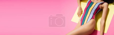 top view of cropped african american woman in colorful swimsuit getting tan on yellow and pink background, banner 