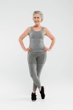 Foto de Longitud completa de mujer alegre y jubilada en ropa deportiva posando sobre gris - Imagen libre de derechos