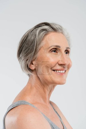 portrait de femme âgée heureuse avec les cheveux gris debout et regardant loin isolé sur gris 