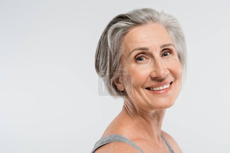 portrait of satisfied senior woman with grey hair looking at camera isolated on grey 