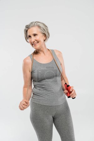 pleased senior woman with grey hair holding skipping rope isolated on grey 
