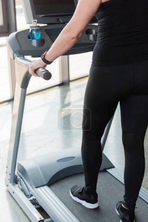 cropped view of senior woman in black leggings running on treadmill 