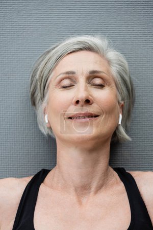Photo for Top view of happy senior woman in wireless earphones lying on fitness mat - Royalty Free Image