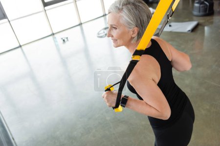 Blick aus der Vogelperspektive auf eine lächelnde Seniorin in Sportkleidung, die mit Federbeinen im Fitnessstudio trainiert 