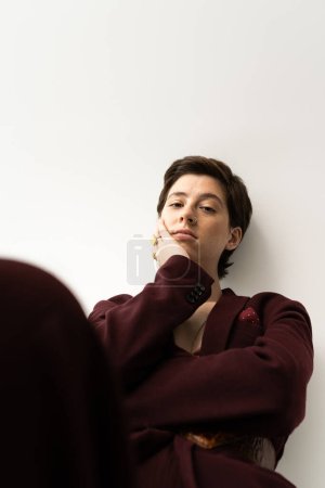 pensive and fashionable woman holding hand near face and looking at camera on grey background