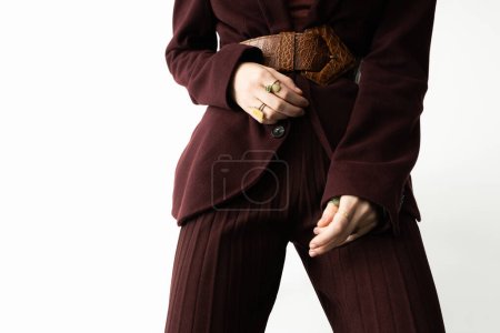 partial view of stylish woman in brown pantsuit and leather belt on white background