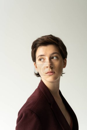 Téléchargez les photos : Portrait de femme brune coûteuse aux cheveux courts regardant loin isolé sur gris - en image libre de droit