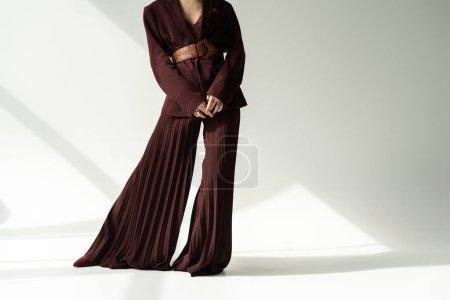Foto de Vista parcial de mujer en pantalones anchos y blazer con cinturón de cuero sobre fondo gris con iluminación - Imagen libre de derechos